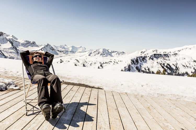 Austria, damuels, woman relaxing in deckchair on sun deck in winter landscape
