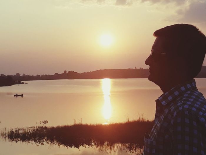Side view of man looking at lake against sky during sunset