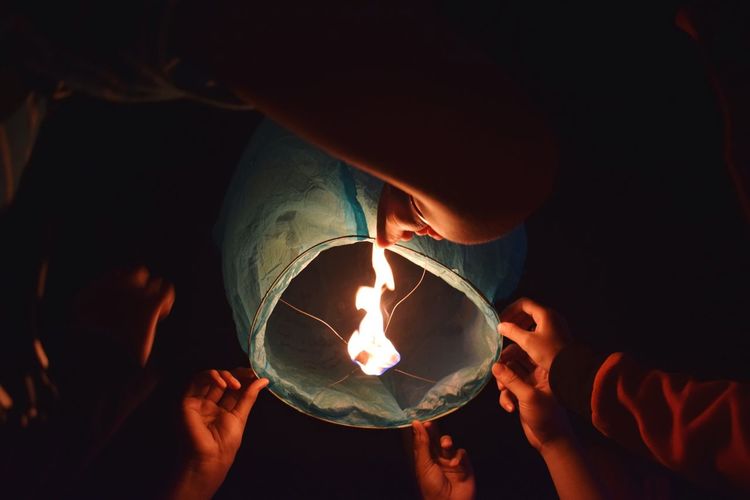 Cropped hands of friends holding lit paper lantern at night
