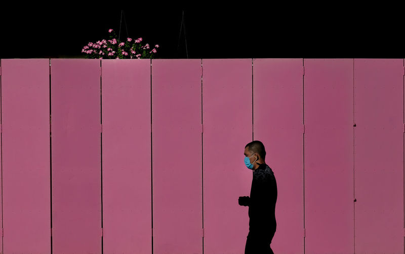 Side view of young man standing against pink wall