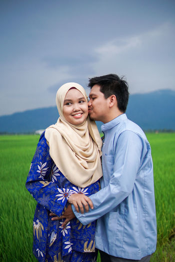 Smiling young couple standing on field against sky