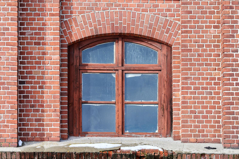 One arched glass window on old red brick wall. window in brown wooden frame on brick wall