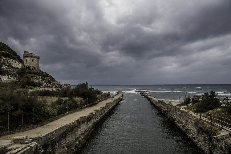 View of road by sea against cloudy sky