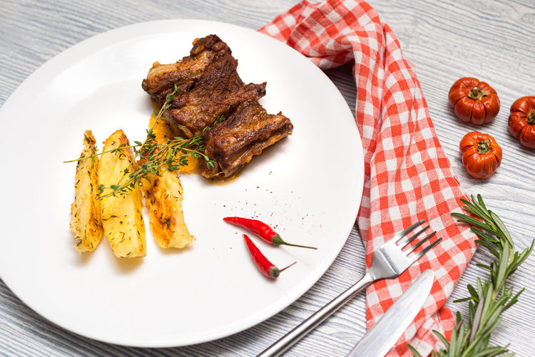 Fried lamb ribs with baked potatoes slices. thyme herbs. one portion on a big white plate.