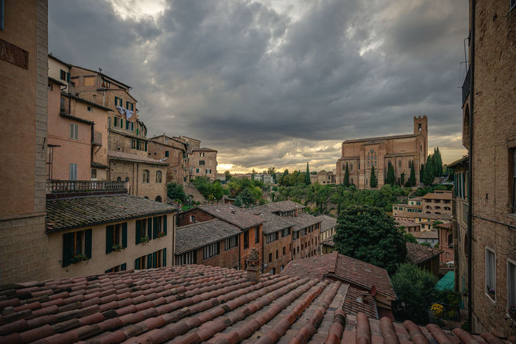 Buildings in city, view over old town shows basilica against cloudy sky, siena italy