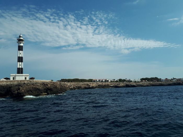 Menorca - spain / lighthouse amidst sea and buildings against sky