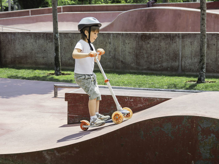 Little boy rides kick scooter in skate park. special concrete bowl in urban park. training to skate.