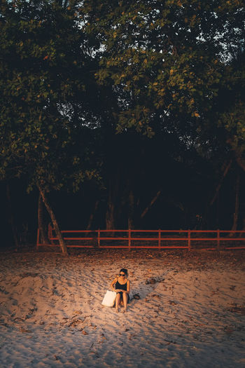 Woman relaxing on sand against trees at beach