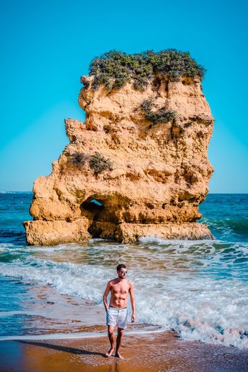 Full length of shirtless man standing on beach against clear sky
