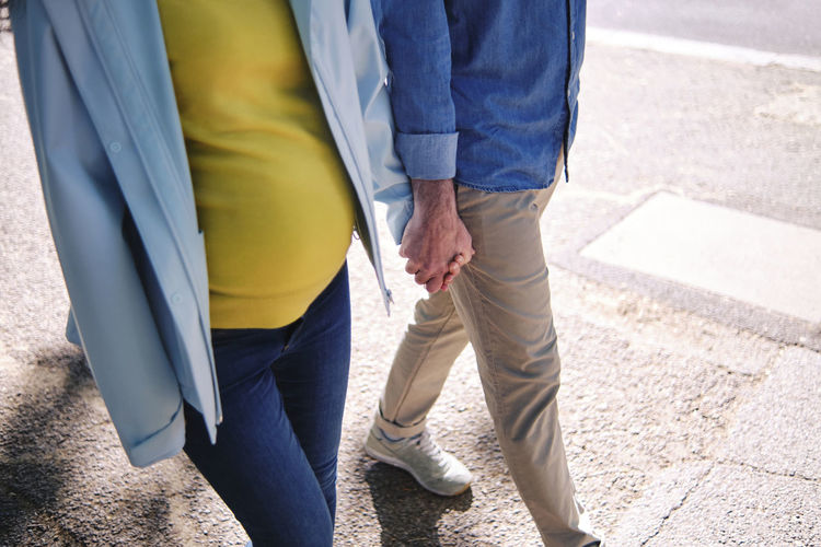 Pregnant woman holding hand of husband while walking on street