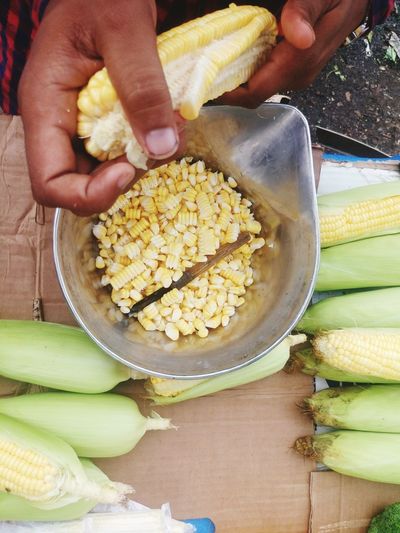 Cropped image of vendor holding corn over container