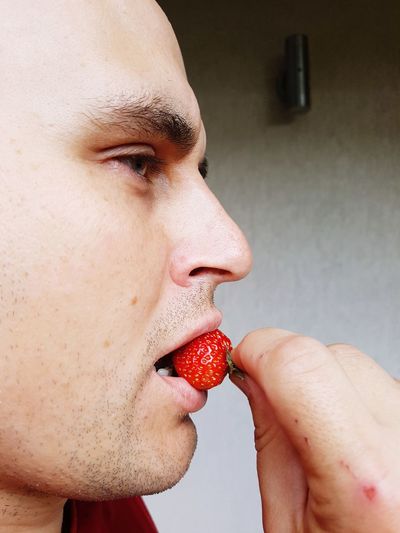 Side view of mid adult man eating strawberry against wall