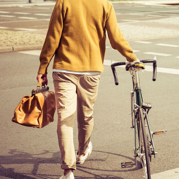 Low section rear view of man carrying bag while walking with bicycle in city