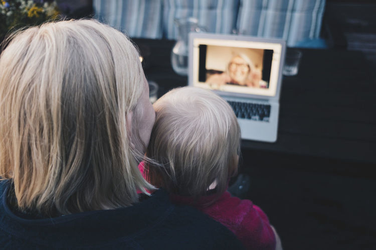 Rear view of mother and daughter doing video conference on laptop at holiday villa