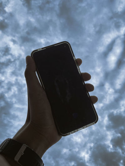Low angle view of person using mobile phone against sky