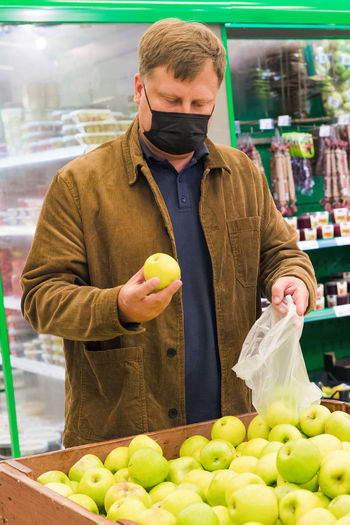 An adult man in a black protective mask in a shopping center chooses fruit.