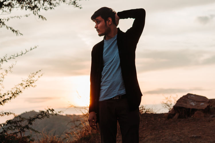 Man looking away while standing on mountain against sky during sunset
