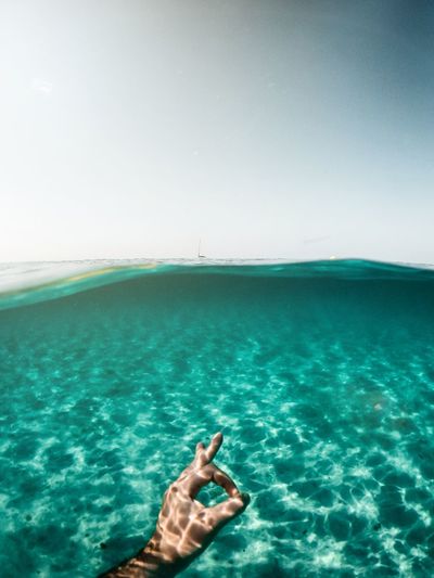 Low section of man relaxing in sea against clear sky