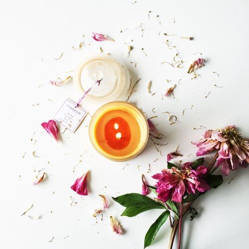 High angle view of lit candle with wilted flowers on white table