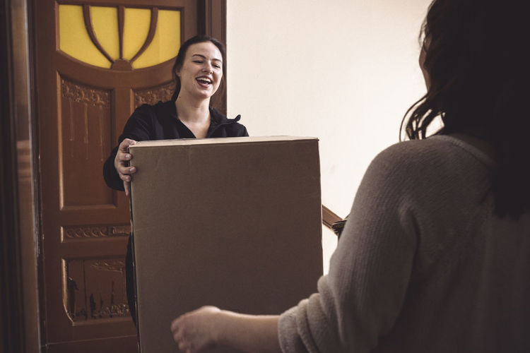Smiling delivery woman making home delivery to female customer at doorstep
