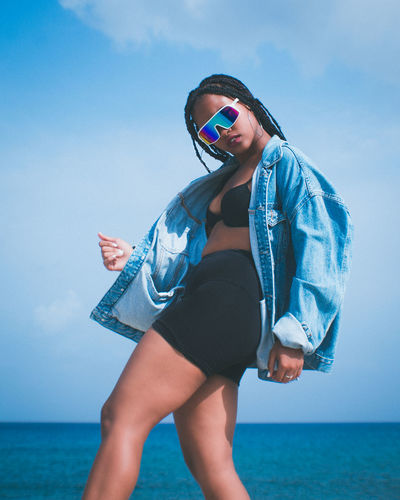 Young woman wearing sunglasses standing by sea against sky