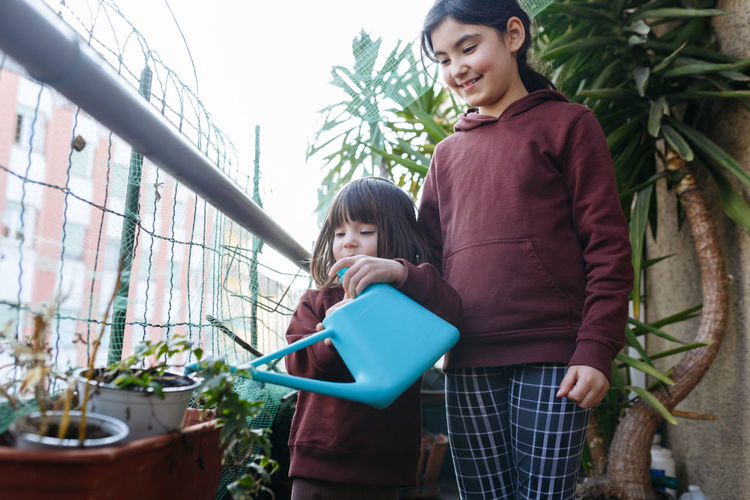 Two sisters with dark hair on apartment balcony watering the plants