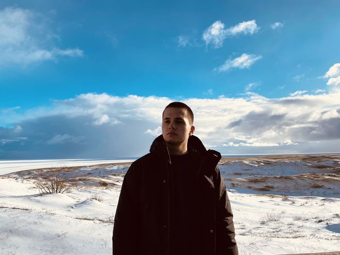 Young man standing on winter beach against sky