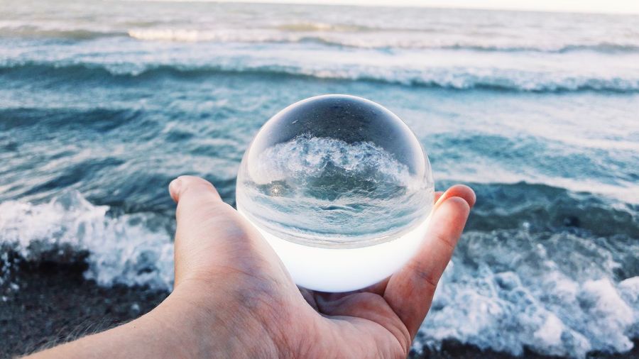 Midsection of person holding crystal ball in sea