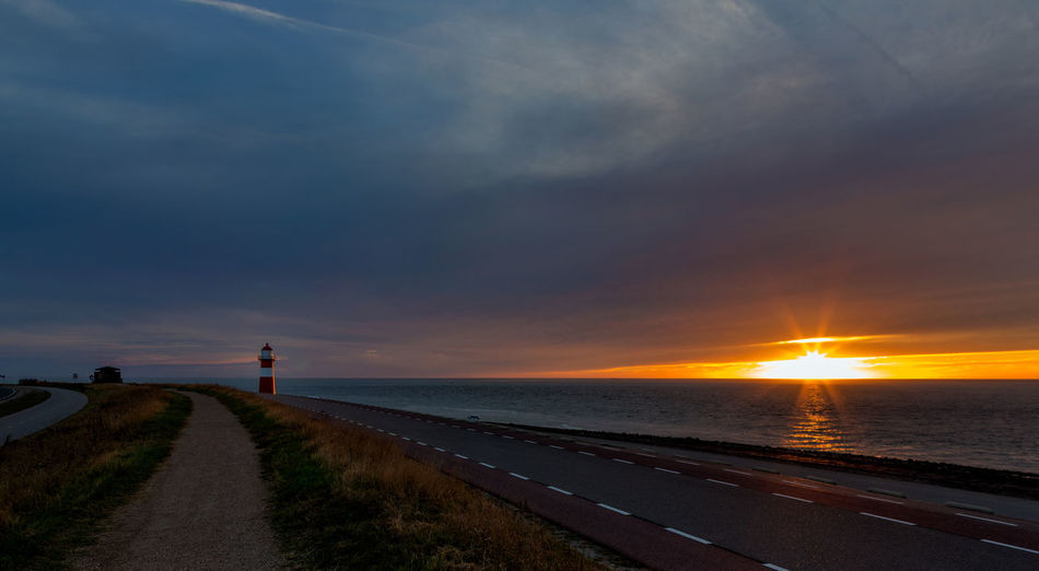 Scenic view of road by sea against sky during sunset