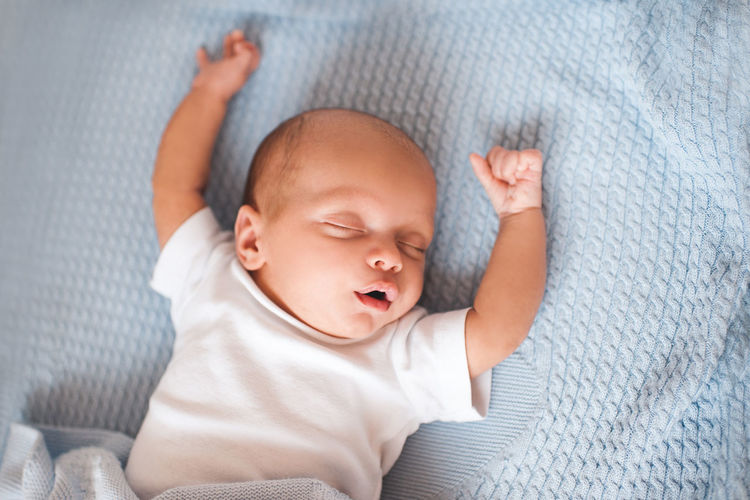 Newborn baby stretching arms on bed