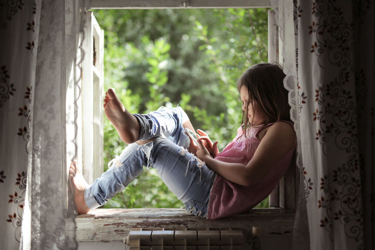 Side view of woman sitting on window