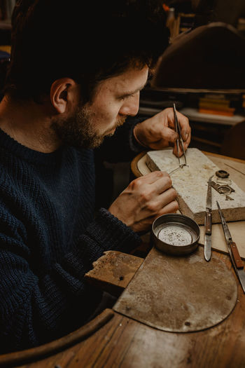 Hands of goldsmith cutting metal with saw while making jewellery in workshop