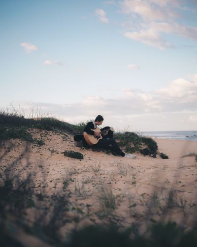 Man playing guitar at beach against sky