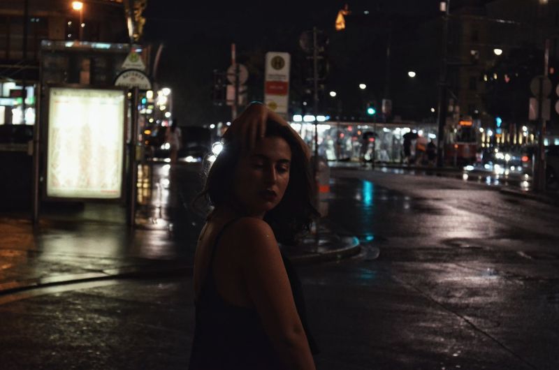 Portrait of woman standing on illuminated street in city at night