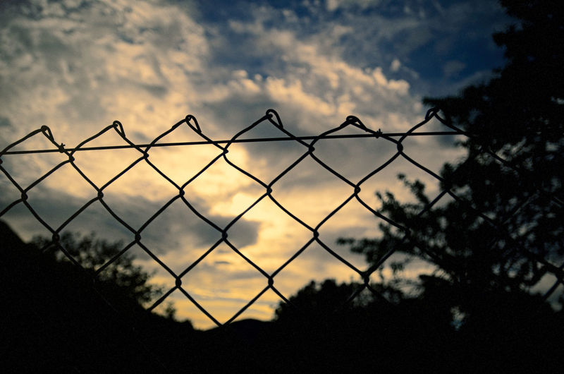 Close-up of silhouette chainlink fence against sky during sunset