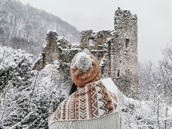 Rear view of young woman in winter clothes looking at castle ruins in winter, snow.