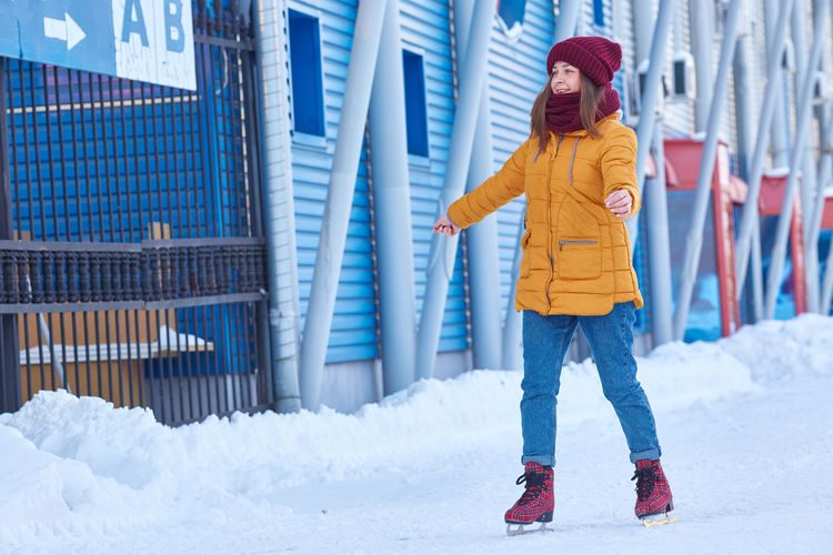 Young woman is skating on the background of a large blue building.