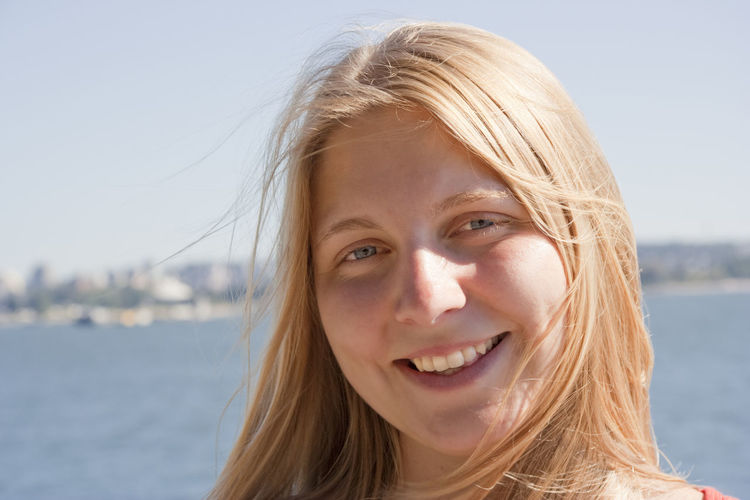 Close-up portrait of smiling young woman against lake at stanley park during sunny day
