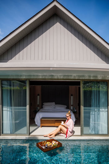 Full length of woman sitting in house by swimming pool