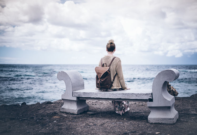 Rear view of woman sitting on bench by sea against sky
