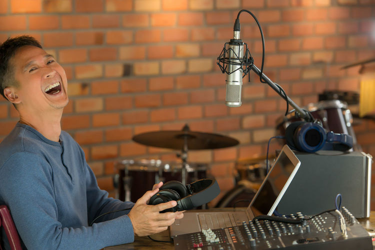 Portrait of happy man sitting by audio equipment at recording studio