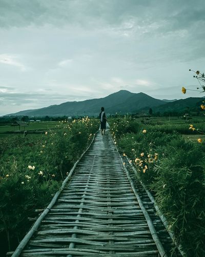 Rear view of man on dirt road amidst mountains against sky