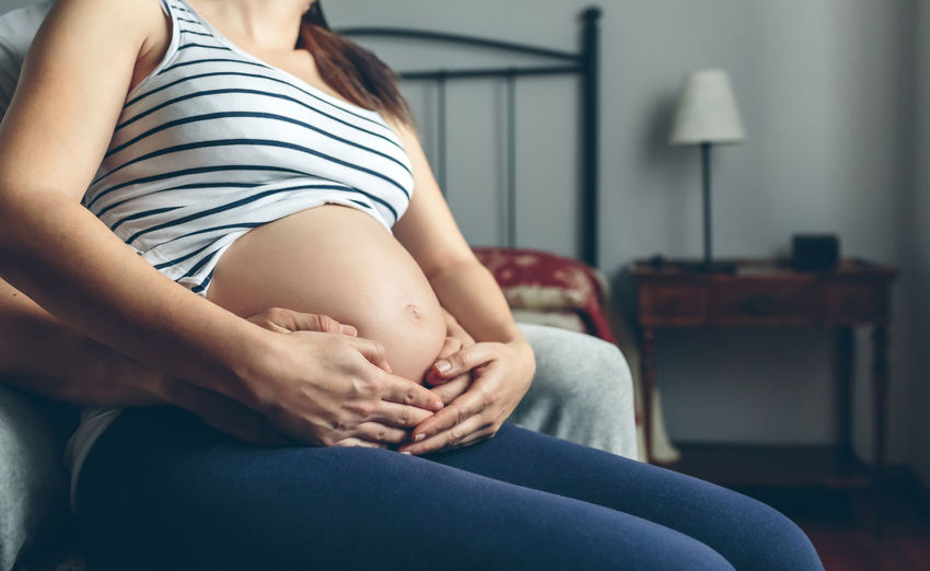 Man embracing pregnant women while sitting on bed at home