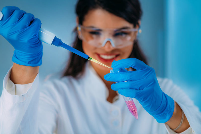 Student in white coat, working in research laboratory using micro pipette and test tube