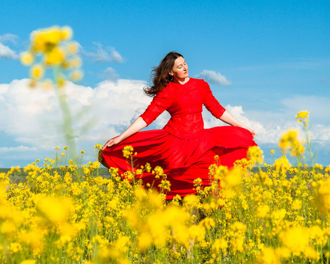 Young woman standing amidst yellow flowering plants on field against sky