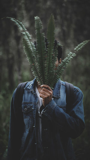 Man covering face with plants in forest