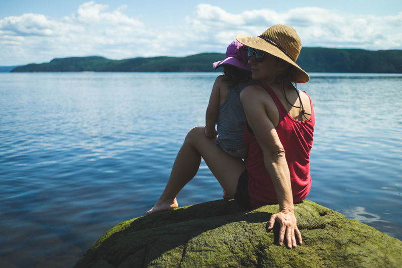 Mother sitting on rock with daughter in arms by lake