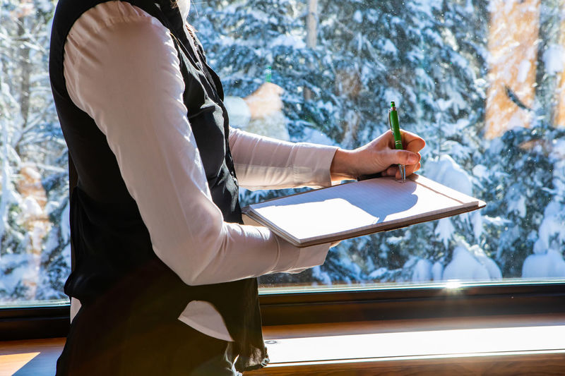 Midsection of woman writing on notepad at home