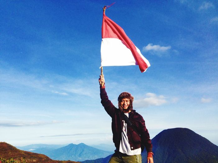Portrait of confident young man holding monaco flag on mountain against sky