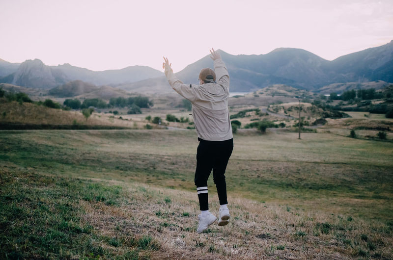 Back view of unrecognizable male in casual clothes jumping high against mountains